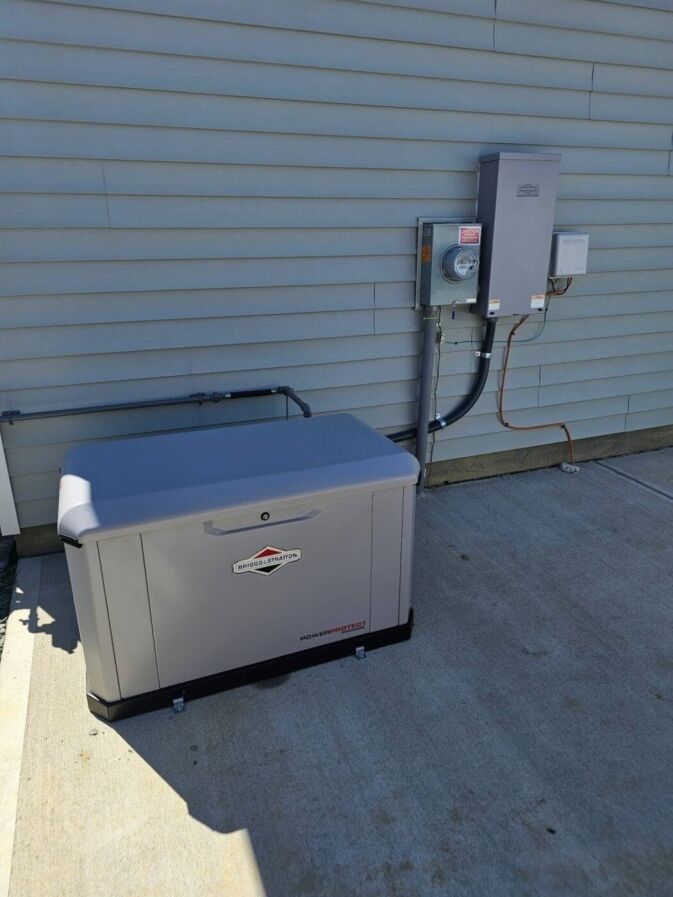 A Briggs & Stratton standby generator is installed on a concrete pad next to an exterior wall, connected to an electrical panel and meter.