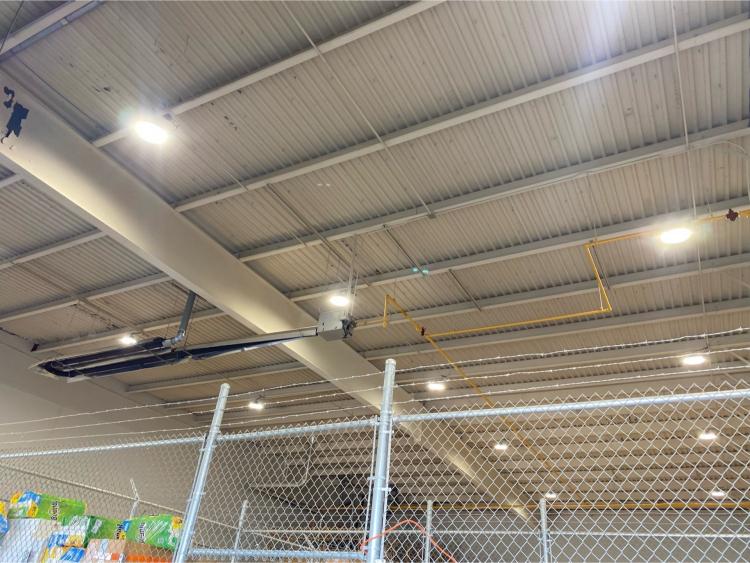 Exposed metal ceiling with overhead lights, pipes, and a fenced area below&mdash;perfect for an electrician working inside an industrial or warehouse space.