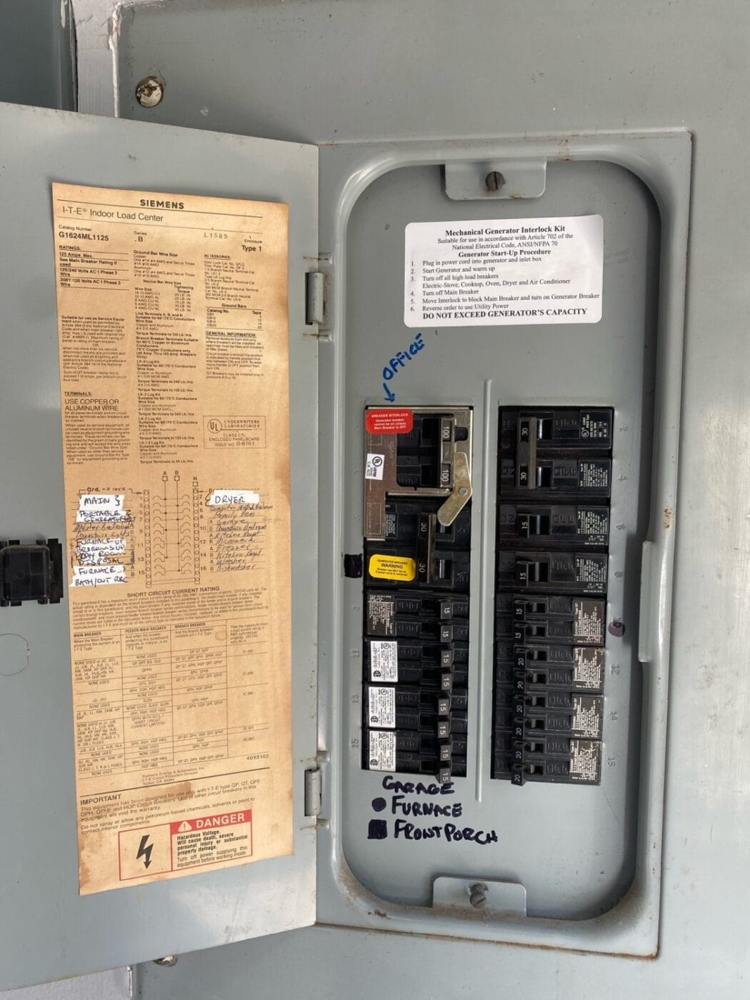 Electrical breaker panel with labeled switches; handwritten notes indicate breakers for garage, furnace, and front porch. Instruction labels and manufacturer details are visible inside the door.