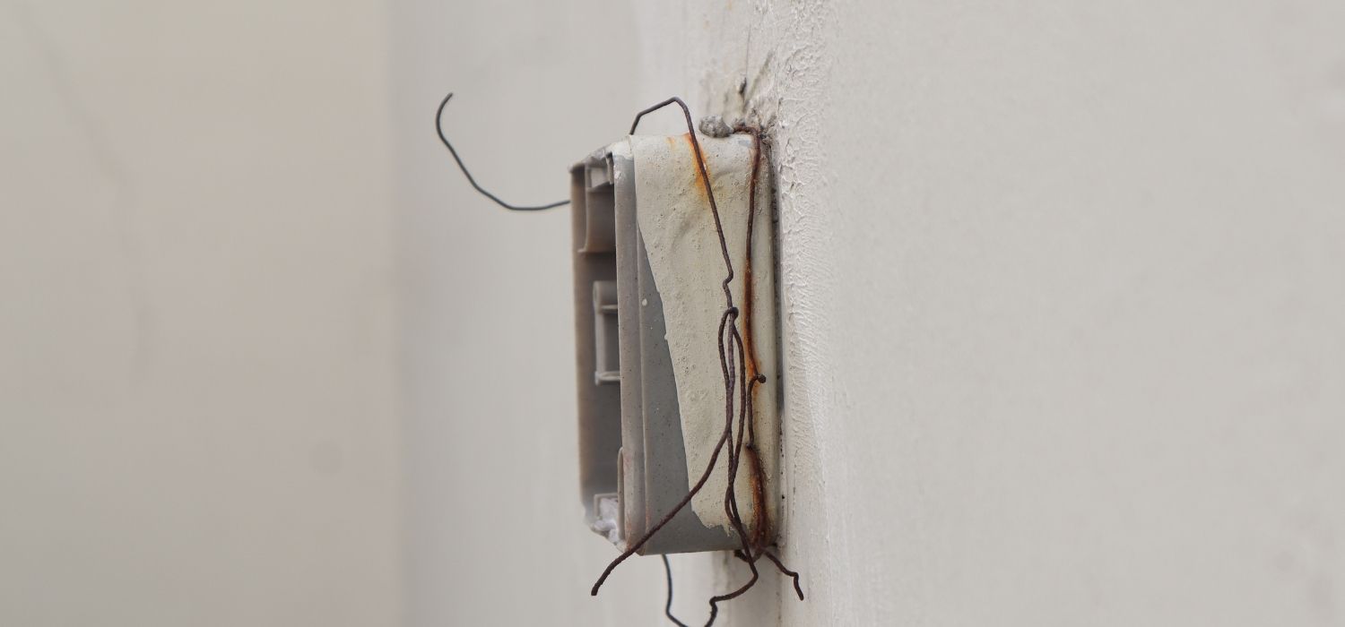 A close-up of a damaged light switch on a white wall with exposed rusty wires sticking out, highlighting the need for an electrical inspection in Fuquay-Varina NC.